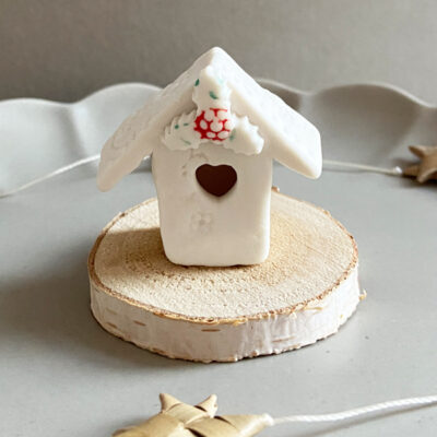 A mini holly house on a wooden base with heart cut out window